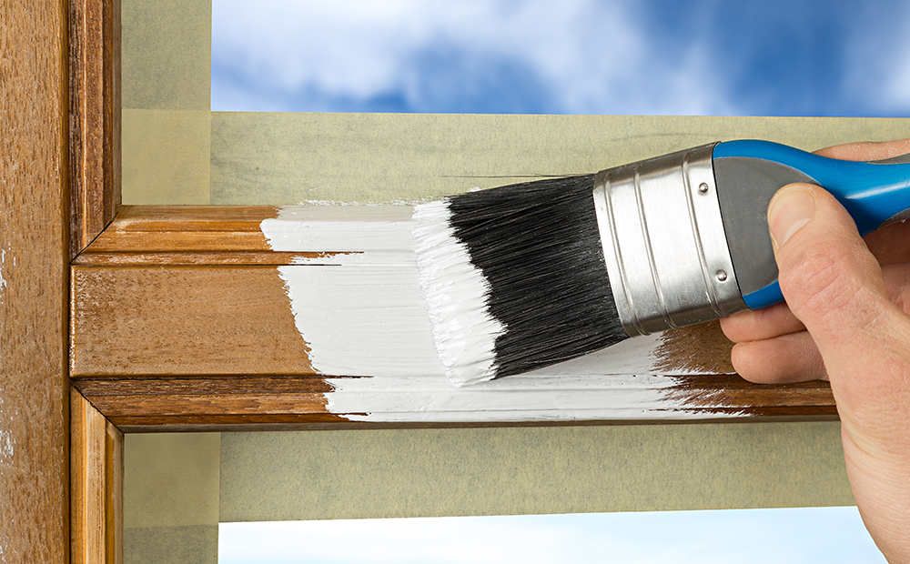 Usuario sosteniendo brocha con pintura blanca sobre marco de madera de una ventana