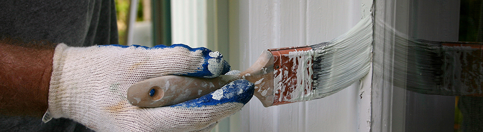 Usuario con guante blanco sosteniendo brocha y pintando el lado izquierdo de un marco de ventana