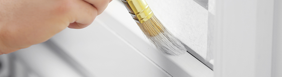 Usuario sosteniendo brocha delgada y pintando marco de ventana color blanco