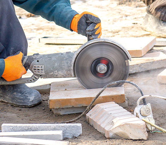 Usuario con guantes de trabajo utilizando sierra circular industrial para cortar un trozo de cemento